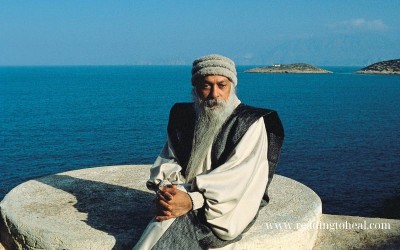 Osho sitting by the blue ocean in a meditative pose